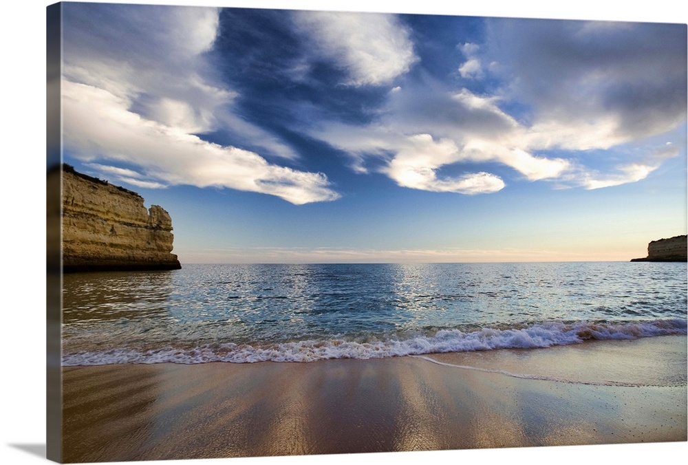 A beautiful picture taken while standing on a beach and looking out at the vast ocean. Cliffs line both sides of the pictu...