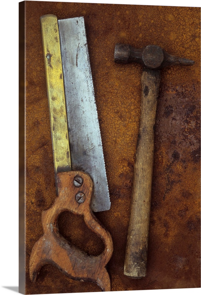 Old well-used tenon saw with wooden handle and brass stiffening bar lying with hammer on rusty metal sheet