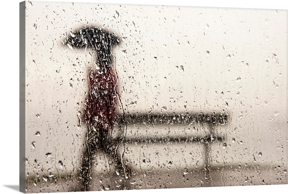 A man walking with an umbrella against a rain streaked window.