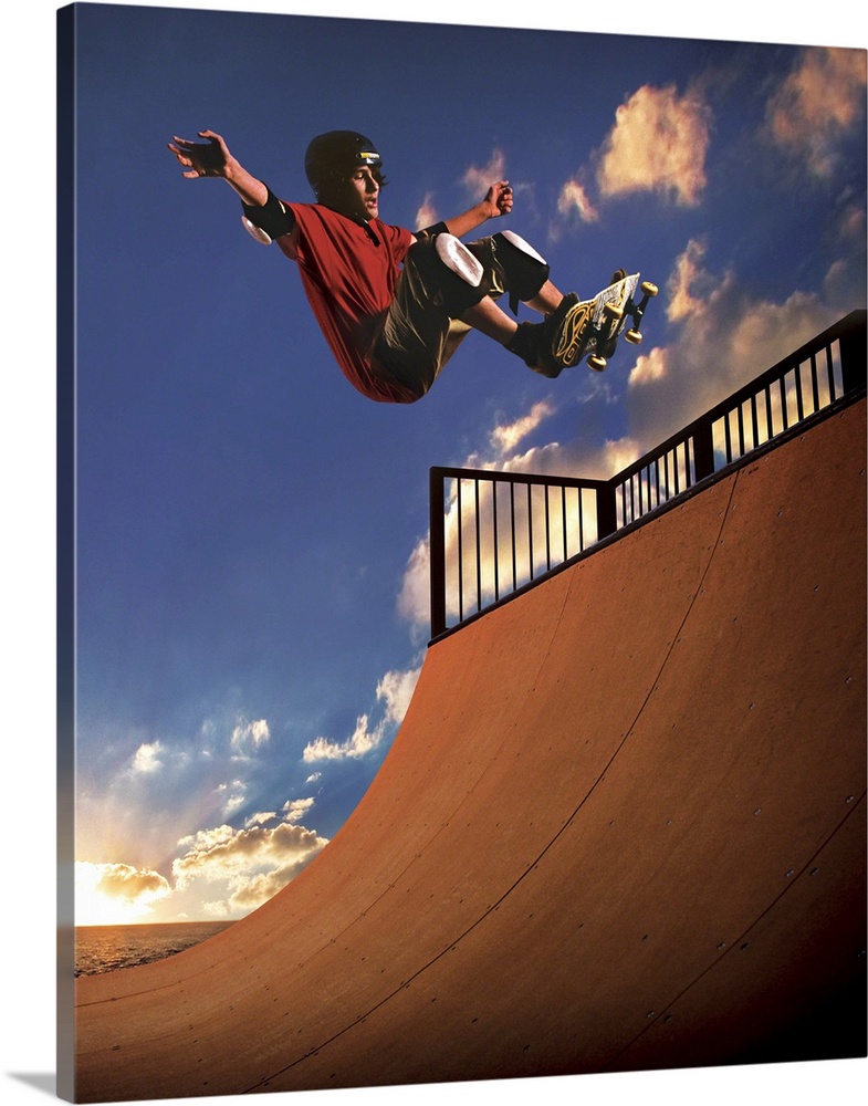 A young boy gets air on his skateboard while skating on a mini ramp at sunset