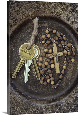 Three brass doorkeys tied with string lying next to rosary with crucifix in old bowl