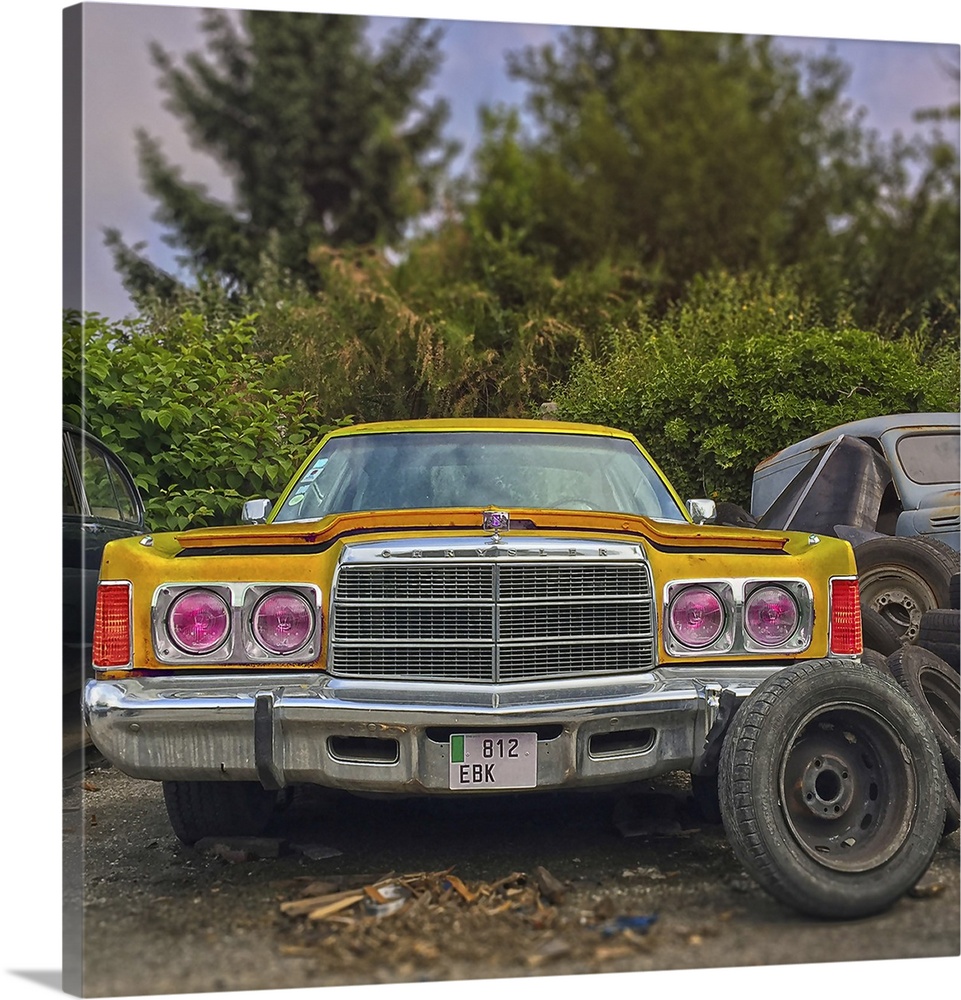 Old yellow classic Chrysler car in salvage area in USA with spare wheels.