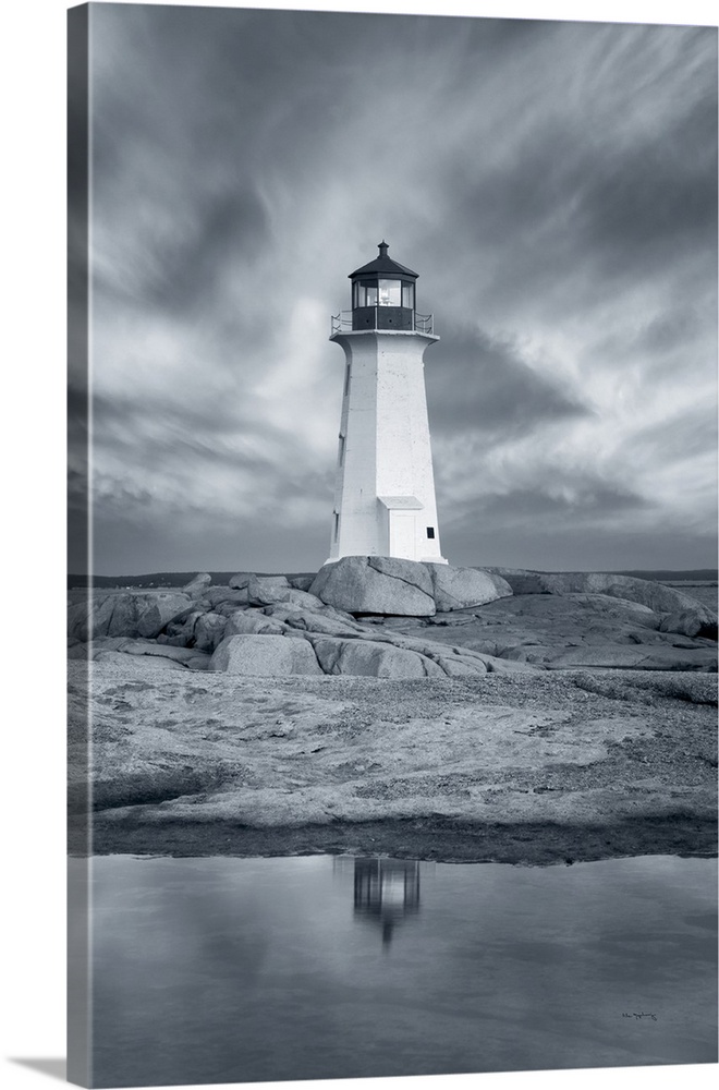 A vertical black and white photograph of a white lighthouse reflecting in the water with a dramatic cloudy sky.