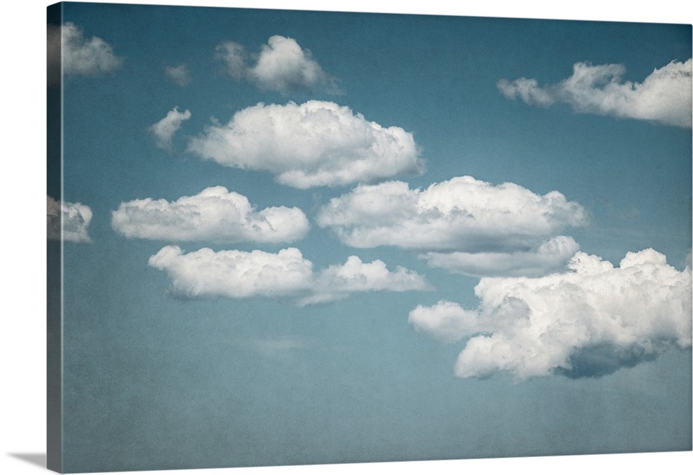 A contemporary photograph of fluffy white clouds against a pale blue sky.