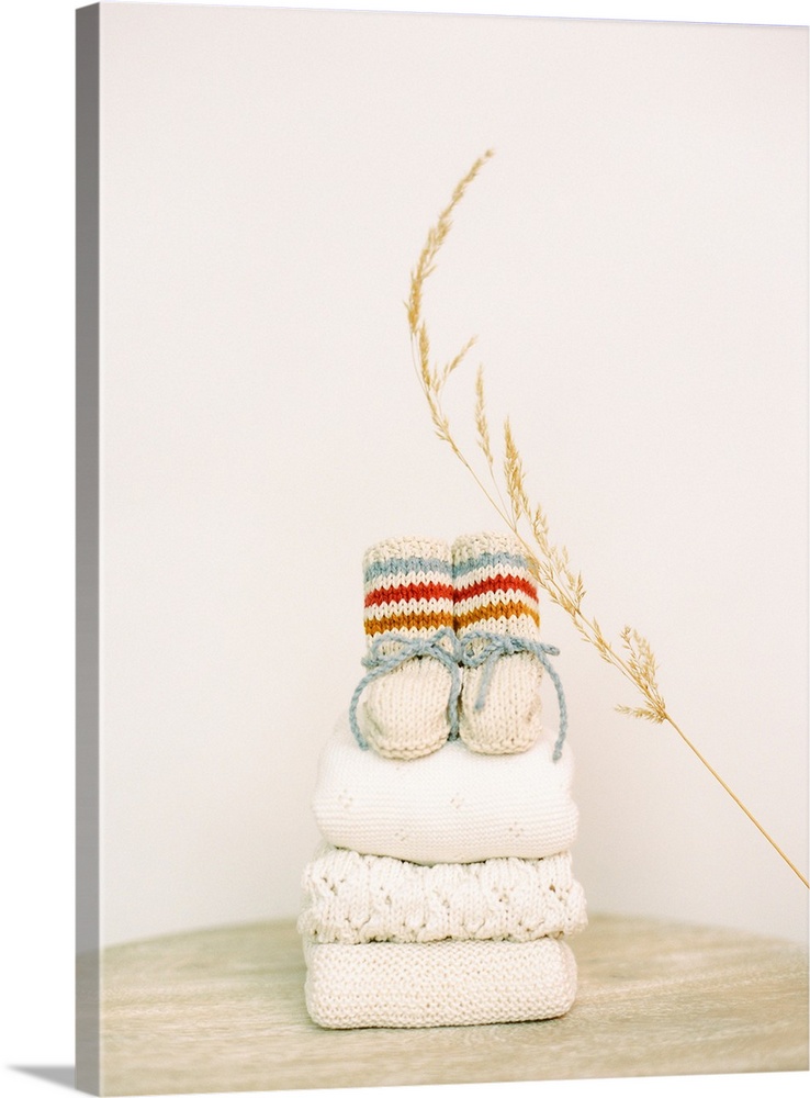 Photograph of knitted booties on top of a pile of folded baby blankets.
