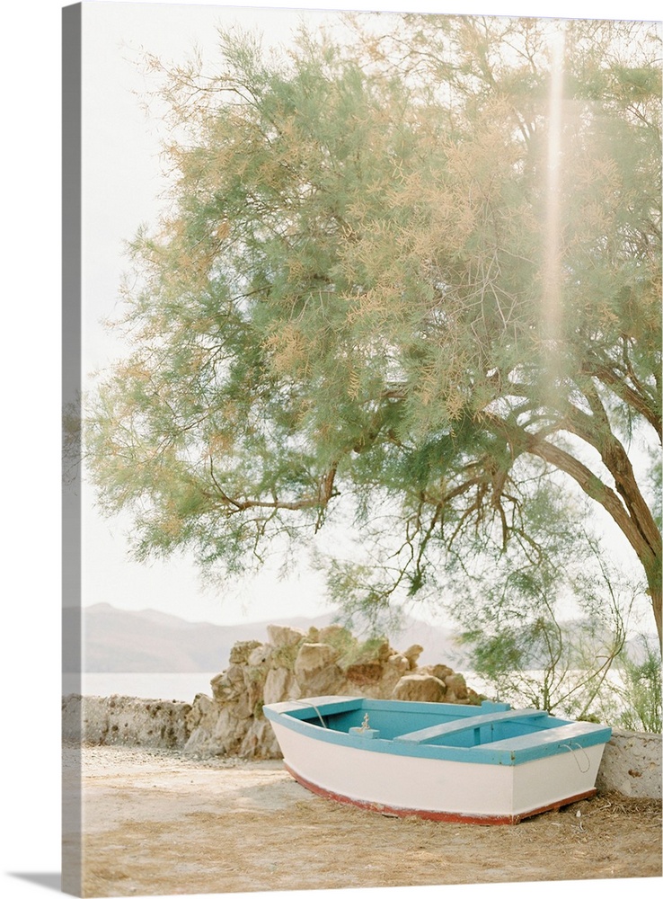 Photograph of a small wooden boat underneath a tree next to the water, Milos, Greece.