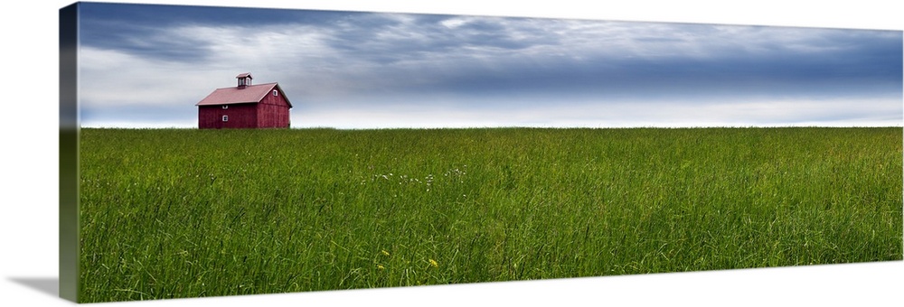 Panoramic photograph of a rural landscape with a wide open green field, red barn, and a blue cloudy sky.