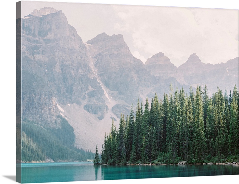 Photograph of tall evergreen trees at the edge of a clear blue lake, Moraine Lake, Banff national park, Canada.