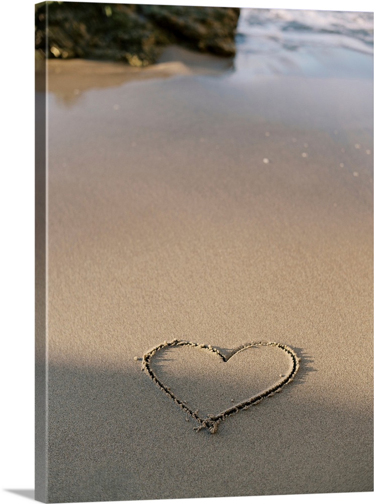 A photograph of a simple heart shape carved into otherwise untouched sand at the edge of the ocean.