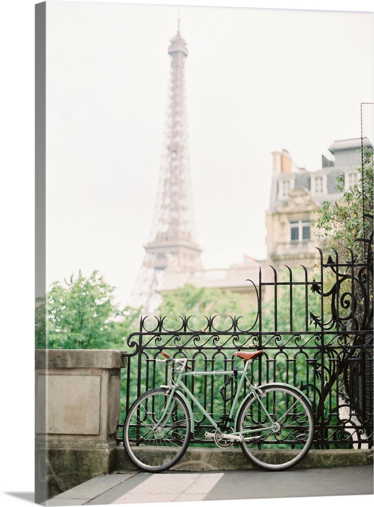 Photograph of a bicycle leaning against an ornate metal railing with the Eiffel tower in the distance.