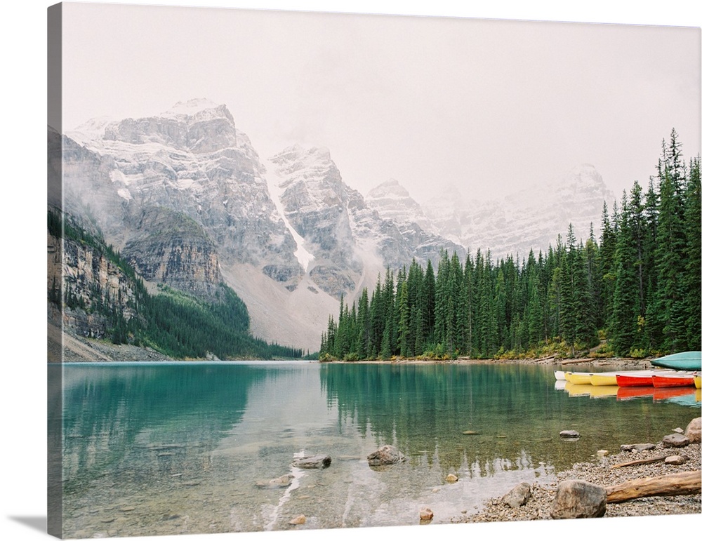 A horizontal photograph of the mountains and trees reflected in Moraine Lake, Banff national park, Canada.