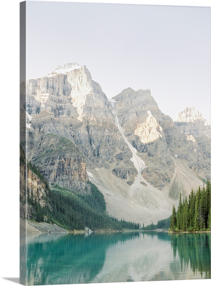 A vertical photograph of the mountains and trees reflected in Moraine Lake, Banff national park, Canada.