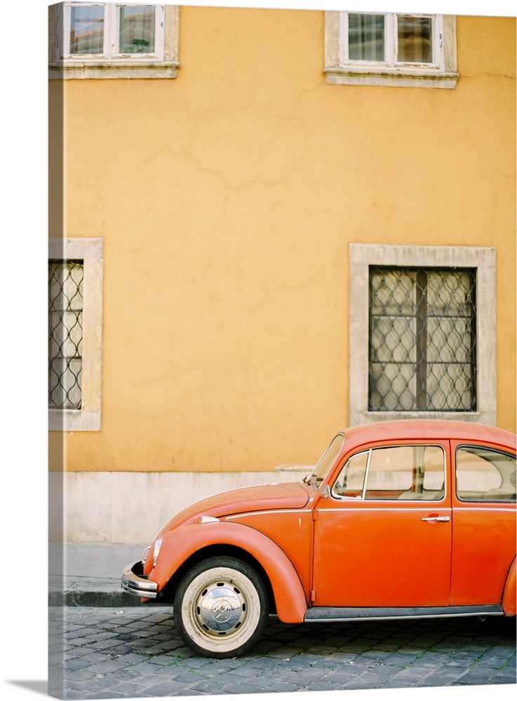 Photograph of an orange Volkswagen Beetle car parked in front of a yellow wall, Budapest, Hungary.