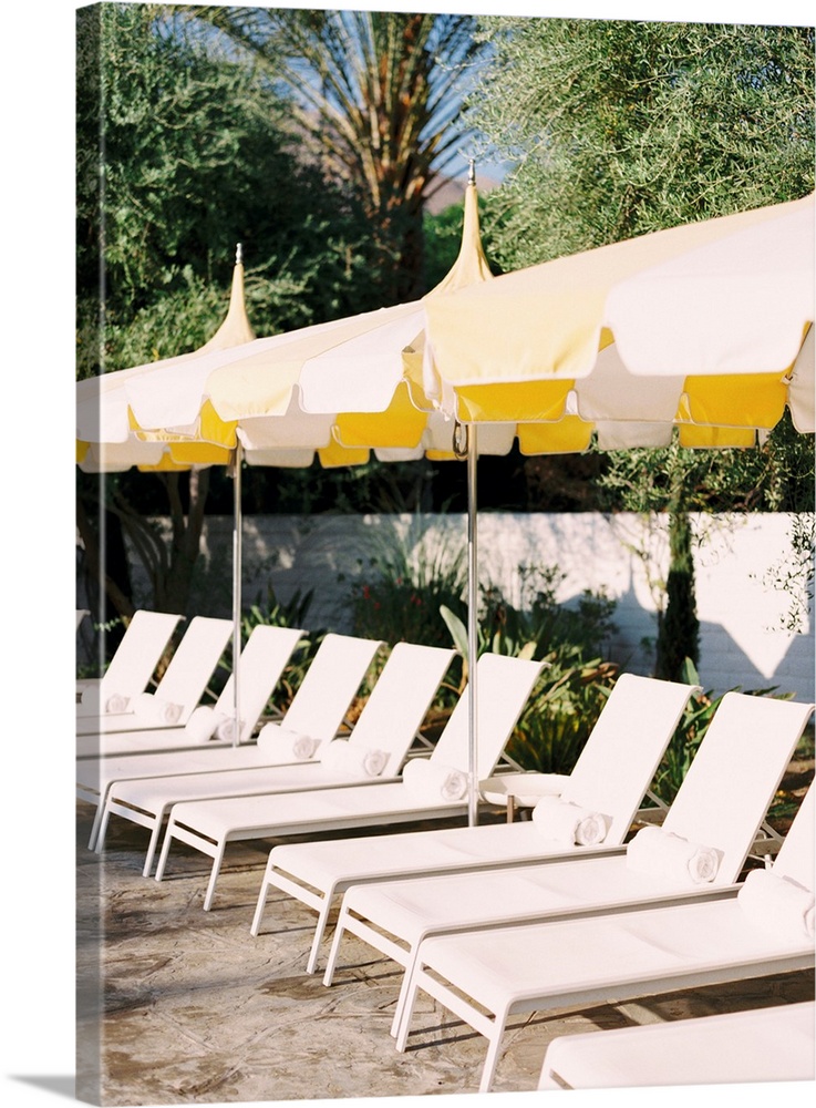 Photograph of a neat row of pool loungers with rolled towels underneath yellow umbrellas.