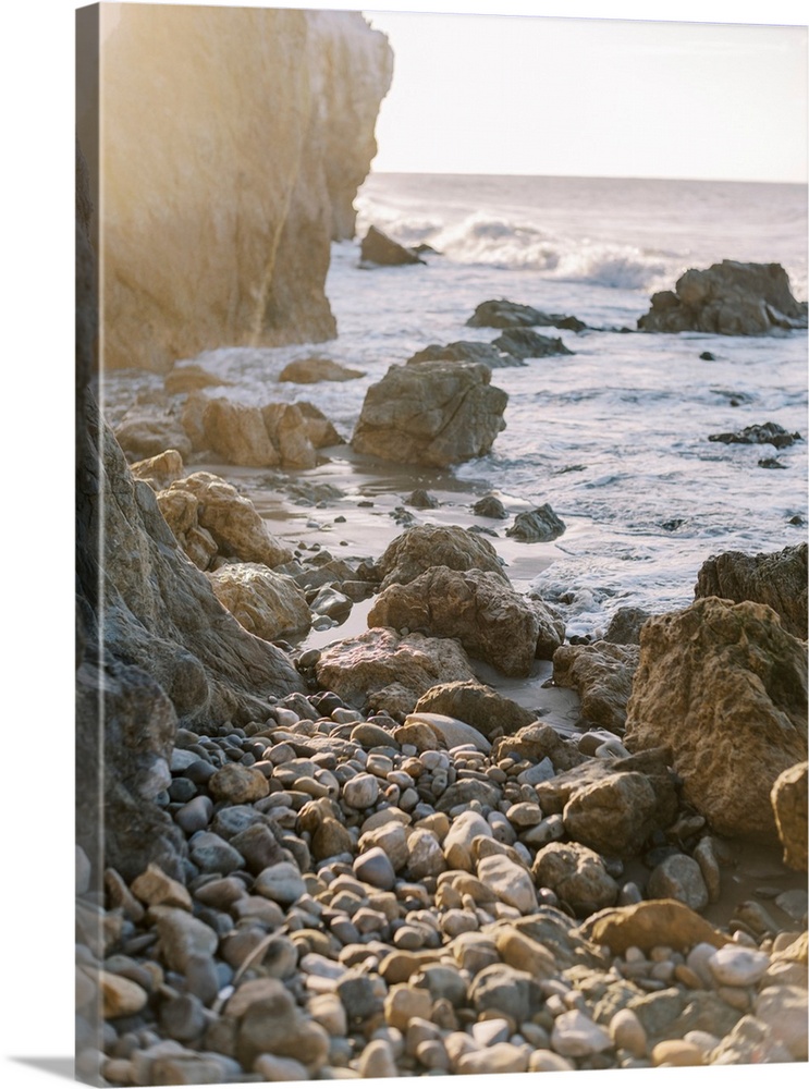A photograph of rocks and boulders at the edge of a rugged coastline at sunset.