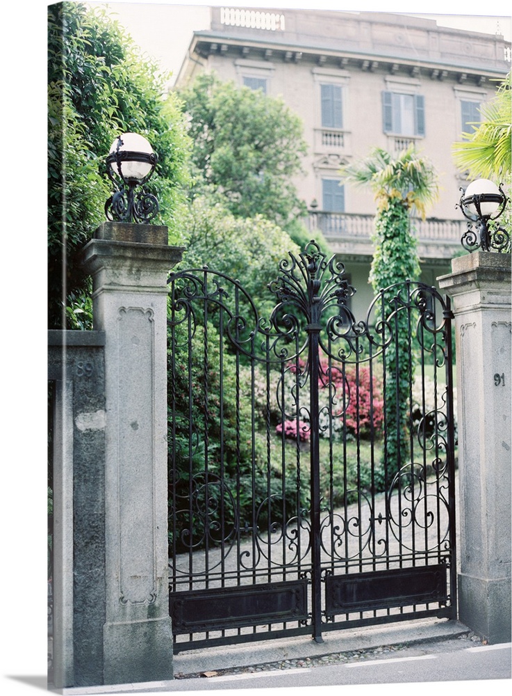 A photograph of a pair of ornate iron gates in front of a mediterranean villa.