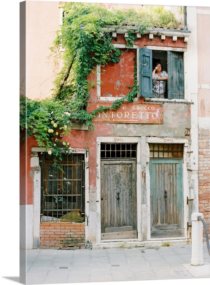 Photograph of a woman looking out of the window of a very old building, Venice, Italy.