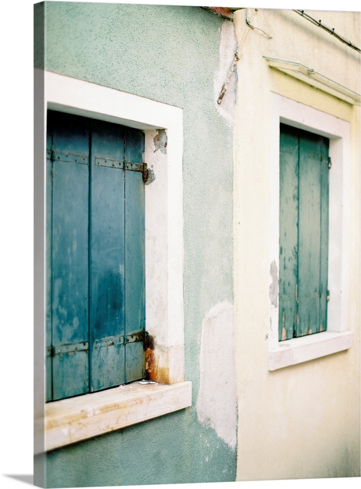 Photograph of a blue house next to a white house, both with old wooden shutters, Burano, Italy.